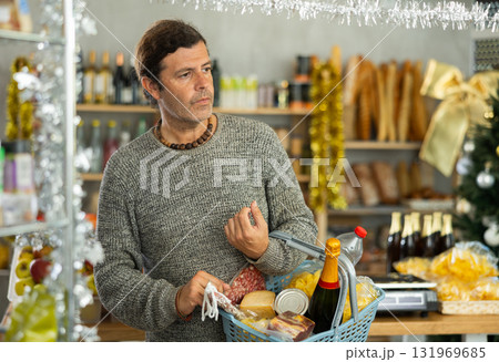 Man with basket shopping in holiday-decorated grocery store Man with basket shopping in holiday-decorated grocery store 131969685