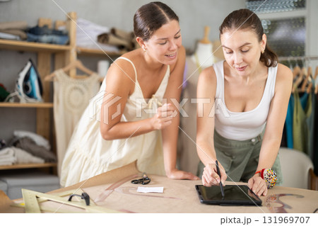 Two female dressmakers drawing a model of clothes on a tablet Two female dressmakers drawing a model of clothes on a tablet 131969707