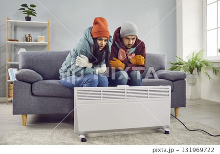 Young frozen couple sitting in the living room at home and trying to keep warm near the heater. 131969722