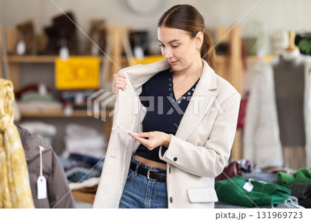Stylish female customer trying new coat in fashionable clothing boutique. Black Friday sale of winter clothing collection Stylish female customer trying new coat in fashionable clothing boutique. Black Friday sale of winter clothing collection 131969723