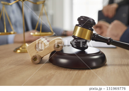 Toy car, sound block, gavel and scales of justice on table, with accident lawyers in background 131969776
