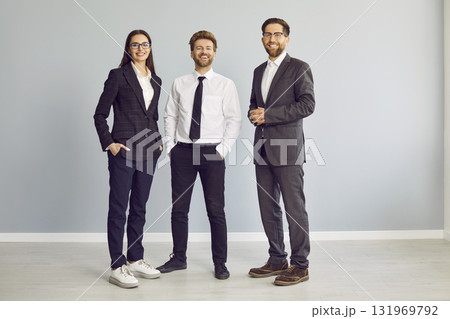 Three cheerful business people standing isolated on grey background and looking at camera. 131969792