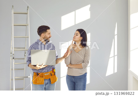 Repairman with a laptop talking to a young woman about things he has to repair in the house Repairman with a laptop talking to a young woman about things he has to repair in the house 131969822