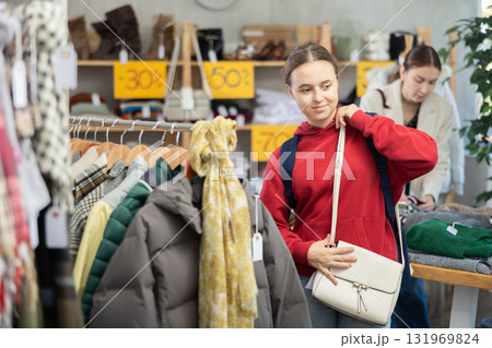 Happy teenage girl choosing ladies' handbag in clothing shop with large assortment 131969824