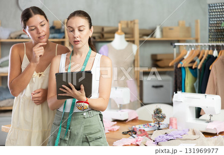 Two female dressmakers drawing a model of clothes on a tablet Two female dressmakers drawing a model of clothes on a tablet 131969977