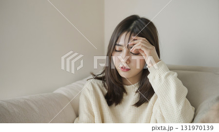 辛そうにソファーに座って頭に片手を当てる若い女性 131970139