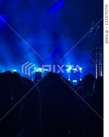 A rock concert with black silhouettes of fans enjoying the musical performance.Blue lights on a blurred stage in the background A rock concert with black silhouettes of fans enjoying the musical performance.Blue lights on a blurred stage in the background 131970259