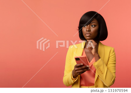 african woman in a yellow suit holds a smartphone, thinking, against a coral background african woman in a yellow suit holds a smartphone, thinking, against a coral background 131970594