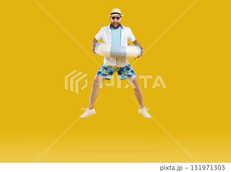 Happy man with inflatable beach ring enjoying summer vacation and jumping on trampoline Happy man with inflatable beach ring enjoying summer vacation and jumping on trampoline 131971303
