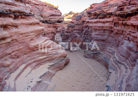 Visitors explore the stunning rock formations and sandy paths of Tsvetnoy Canyon in Egypt under clear blue skies. 131971625