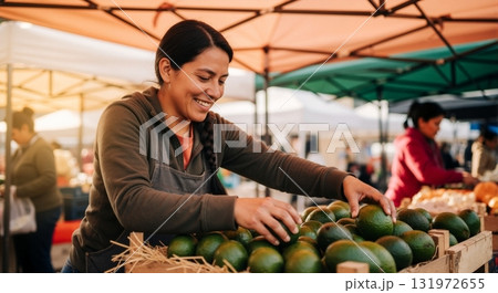 Smiling female vendor sorting fresh avocados at a local farmers market. Hispanic woman working at an outdoor food stall. Small business and healthy eating concept 131972655
