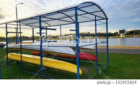 Boats stored under shelter near a calm water body during a sunny afternoon in a recreational area Boats stored under shelter near a calm water body during a sunny afternoon in a recreational area 131972924