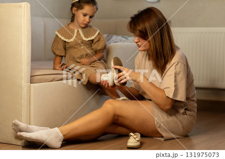 Mother helps daughter put on shoes at home Mother helps daughter put on shoes at home 131975073