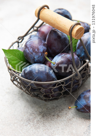 Fresh purple plums in wire basket on concrete 131976048