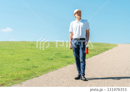 パターとゴルフクラブを持ってゴルフ場を歩く男性 パターとゴルフクラブを持ってゴルフ場を歩く男性 131976353