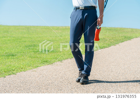パターとゴルフクラブを持ってゴルフ場を歩く男性の足元 131976355