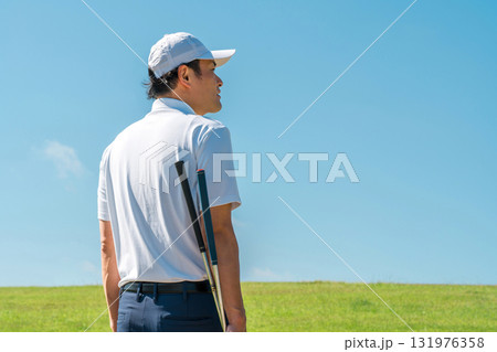 パターとゴルフクラブを持ってゴルフ場を歩く男性の後ろ姿 パターとゴルフクラブを持ってゴルフ場を歩く男性の後ろ姿 131976358