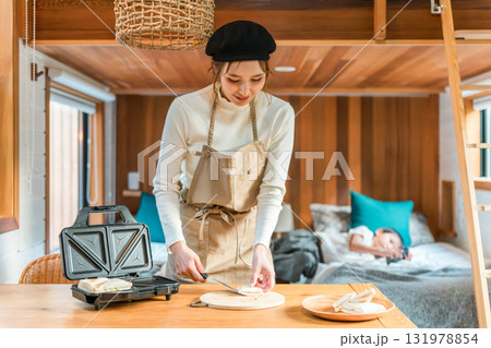 ホットサンドメーカーでホットサンド,サンドイッチを調理するエプロン姿の若いアジア人女性 131978854