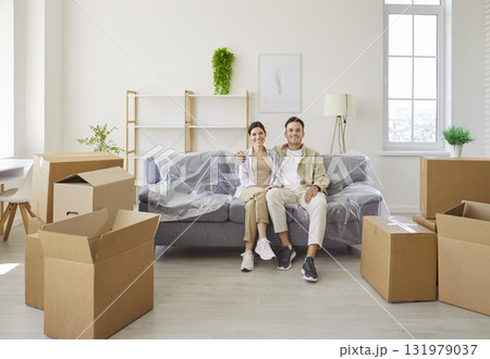 Smiling couple relaxing on sofa, moving cardboard boxes stack on floor Smiling couple relaxing on sofa, moving cardboard boxes stack on floor 131979037