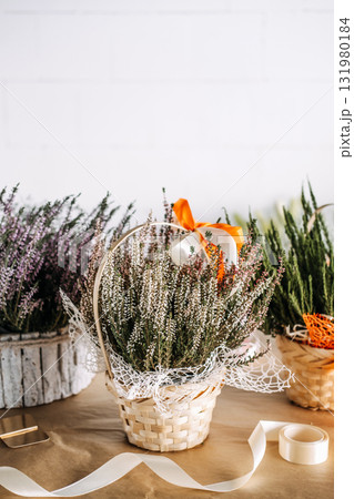 Heather flowers Thanksgiving arranged in a woven basket with white netting and an orange ribbon. Gift giving, sustainable decor, modern rustic design, seasonal celebration Heather flowers Thanksgiving arranged in a woven basket with white netting and an orange ribbon. Gift giving, sustainable decor, modern rustic design, seasonal celebration 131980184