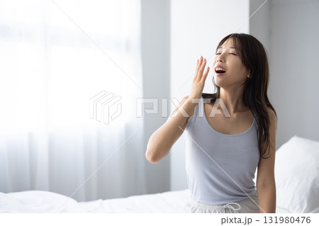 窓からの朝日を浴びながらあくびをする若い女性 窓からの朝日を浴びながらあくびをする若い女性 131980476
