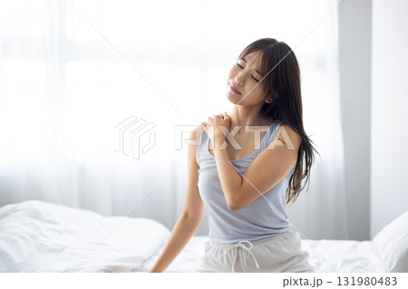 窓からの朝日を浴びながら肩をマッサージする若い女性 131980483