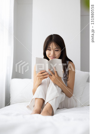 窓からの朝日を浴びながらベッドの上で読書する若い女性若い女性 131980558