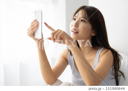 窓からの朝日を浴びながらベッドの上でスマートフォンを操作する若い女性若い女性 窓からの朝日を浴びながらベッドの上でスマートフォンを操作する若い女性若い女性 131980644