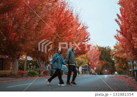 A Couple Walking Hand in Hand Beneath the Vibrant Autumn Trees Surrounding Them A Couple Walking Hand in Hand Beneath the Vibrant Autumn Trees Surrounding Them 131981354