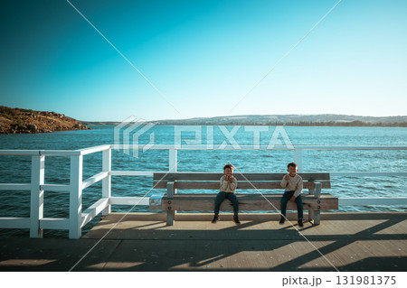 Two Children Are Relaxing and Enjoying Time by the Serene Waterfront 131981375