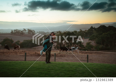 A Joyful Couple Embracing on a Picturesque Farm at Sunset Hour 131981389