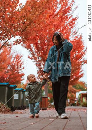 Autumn Stroll: Mother and Child Walking Amidst Colorful Fall Leaves 131981431