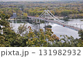 Suspension pedestrian bridge crossing a calm river surrounded by autumn trees. Concept of urban landscape, travel destination, and architectural connection with nature 131982932