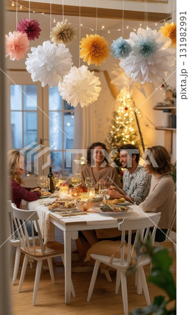 Group of friends enjoying dinner together in a beautifully decorated room with lights and paper flowers Group of friends enjoying dinner together in a beautifully decorated room with lights and paper flowers 131982991