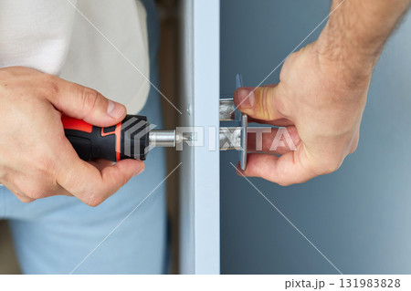 worker installing new handle of cabinet door with screwdriver, close-up. furniture assembly service worker installing new handle of cabinet door with screwdriver, close-up. furniture assembly service 131983828