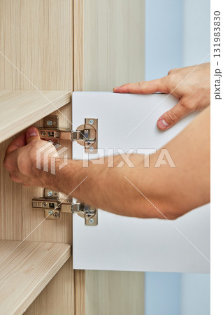 handyman assembling cabinet and screwing door hinge , close-up 131983830