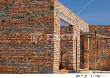Construction workers build a new residential structure with brick walls, showing scaffolding and a clear blue sky above 131983887