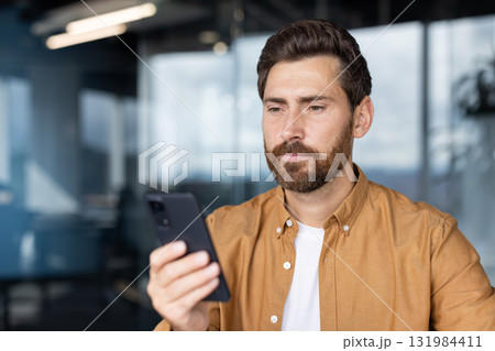Bearded man intently focused on his smartphone, networking and managing business apps in a modern coworking space, checking messages, browsing data and staying connected Bearded man intently focused on his smartphone, networking and managing business apps in a modern coworking space, checking messages, browsing data and staying connected 131984411