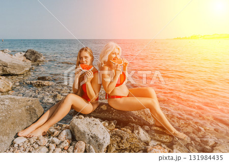 Watermelon Beach Summer: Two women enjoy refreshing watermelon slices by the sea during a sunny summer day. Watermelon Beach Summer: Two women enjoy refreshing watermelon slices by the sea during a sunny summer day. 131984435