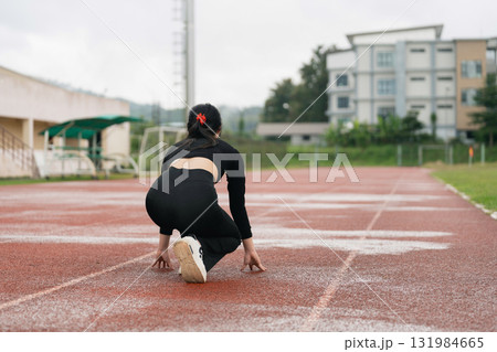 Female Athlete Preparing for Race on Track at Outdoor Stadium, Focus on Sprinting Posture with Determined Expression and Training Environment Female Athlete Preparing for Race on Track at Outdoor Stadium, Focus on Sprinting Posture with Determined Expression and Training Environment 131984665