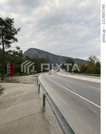 The highway runs along the mountains, cars move along it The highway runs along the mountains, cars move along it 131985349