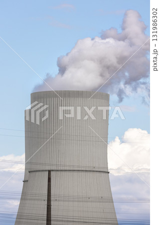 Tall cooling tower releasing steam into blue sky, symbol industrial energy production and technology. The structure represents power generation, heat emission and environmental engineering in Germany 131986302