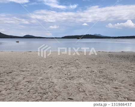 Enjoy a picturesque view of a serene lake, featuring a sandy beach beneath a bright blue sky 131986437