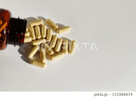 Yellow capsules spill from a brown bottle onto a white background 131986674