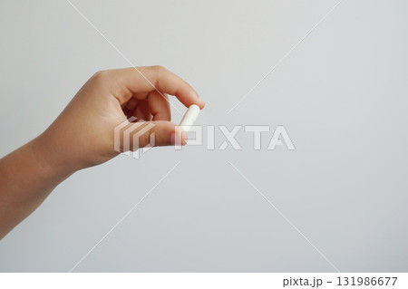 A close-up of a hand holding a white capsule against a light background 131986677