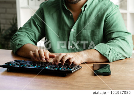 Person typing on keyboard while using smartphone at home office during daytime 131987086