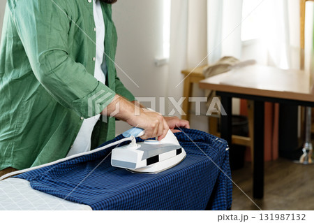 Man ironing a shirt in a bright indoor space during the day 131987132