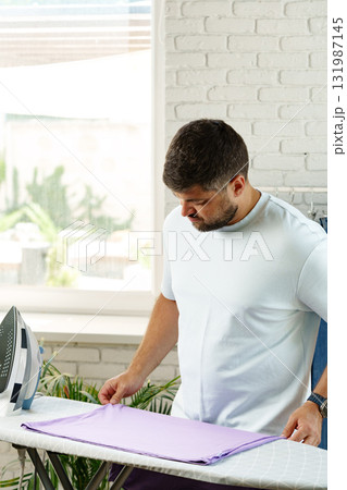 Man ironing a lavender shirt in a bright and modern room with greenery Man ironing a lavender shirt in a bright and modern room with greenery 131987145
