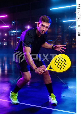 Young athlete prepares to hit a ball with a yellow paddle in a neon-lit indoor court Young athlete prepares to hit a ball with a yellow paddle in a neon-lit indoor court 131987153