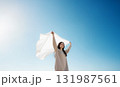 Young woman holding white fabric in bright blue sky, joyful mood 131987561